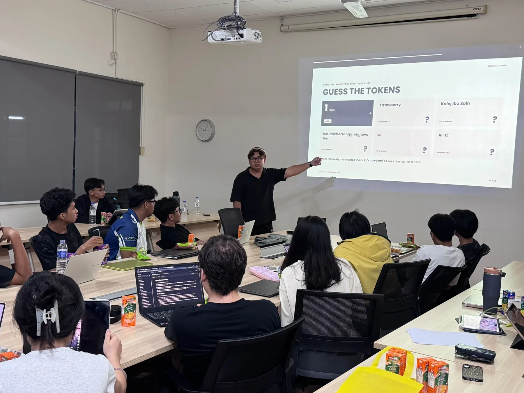 An OrynLab trainer pointing at a 'Guess the tokens' game slide, with participants at laptops